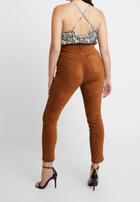 Pantaloni in suede marroni a vita alta con gamba affusolata, abbinati a un top senza maniche con stampa a serpente e spalline incrociate sulla schiena. Tacchi neri.