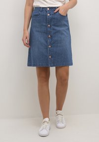 Jeanskjol med vertikala vita ränder, A-linjeform, fem framknappar och sidofickor. Bärs med vita sneakers.