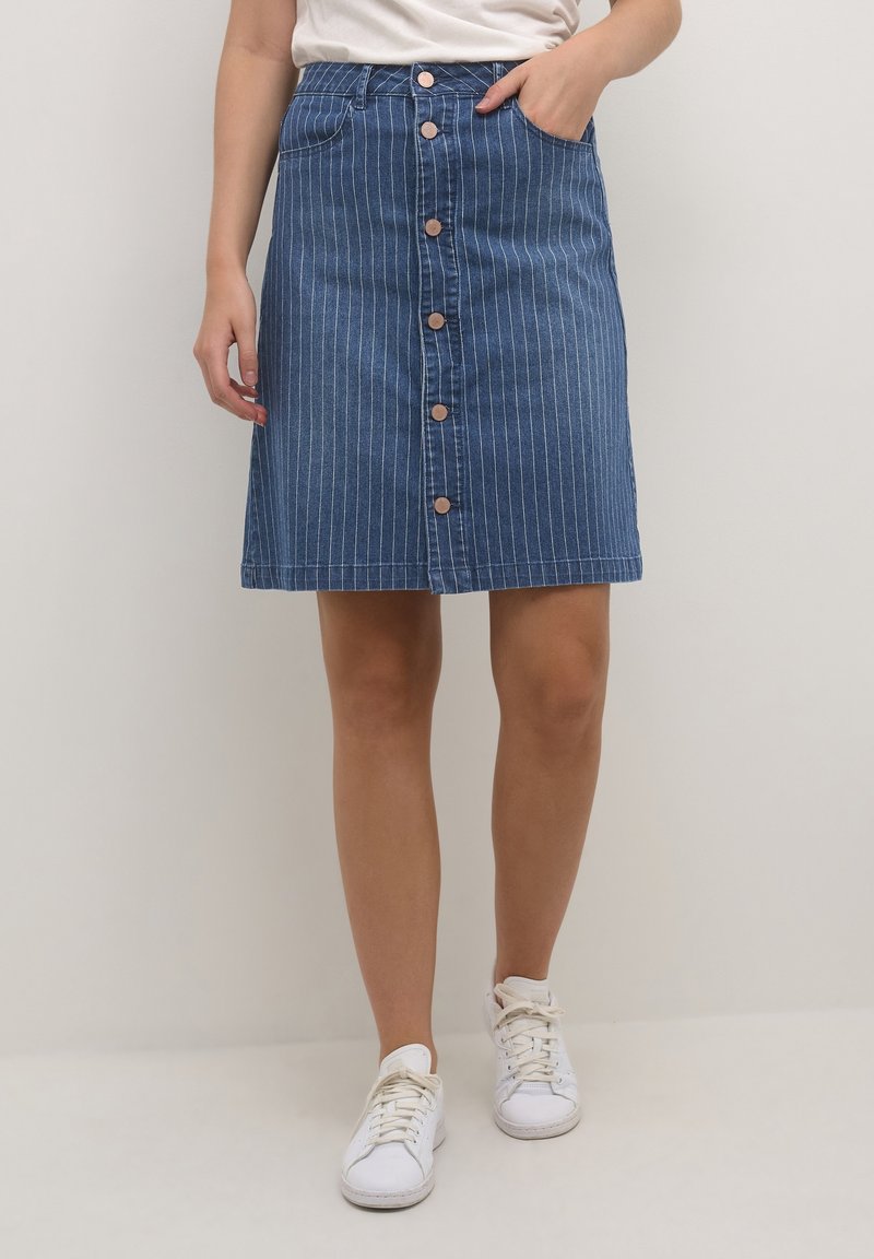 Jeanskjol med vertikala vita ränder, A-linjeform, fem framknappar och sidofickor. Bärs med vita sneakers.