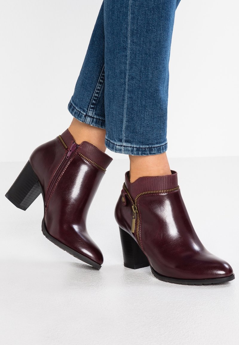 Bottes en cuir bordeaux montant à la cheville avec talons blocs, fermetures éclair sur les côtés, portées avec un jean bleu raccourci.