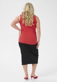 Red sleeveless top paired with a black pencil skirt, featuring smooth fabric and a fitted design. The model wears red high-heeled shoes.
