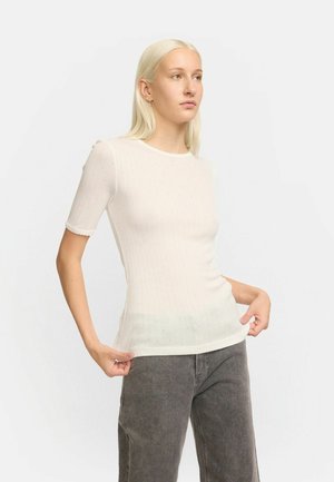 White ribbed short-sleeve top with scalloped cuffs, featuring a subtle dot pattern. Fitted design accentuates the form and texture.