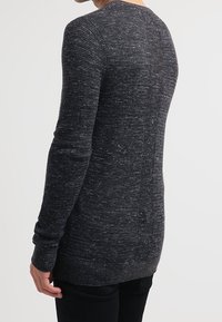 Pull en noir et gris texturé avec un col rond et des manches longues, présentant un motif légèrement chiné et des poignets et un ourlet côtelés.