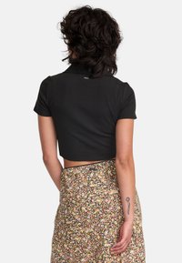 Polo noir cropped à manches courtes ; texture lisse. Associé à une jupe florale avec un fond sombre et des accents de motifs colorés.