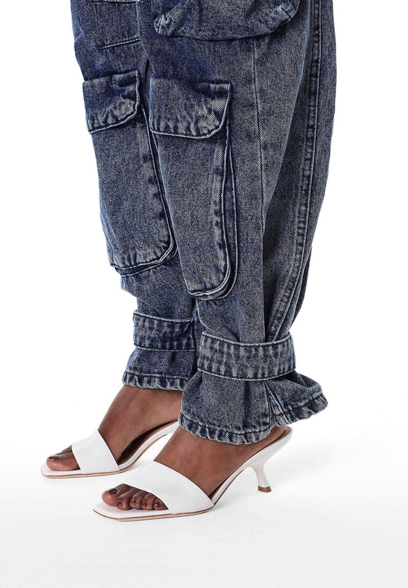 Denim cargobroek met grote zakken en rafelige zomen, gecombineerd met witte open-teenhakken met een strak ontwerp en lage hakken.