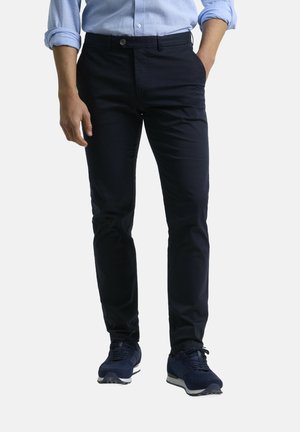 Chinos azul marino fabricados en algodón suave. Cuentan con corte recto, bolsillos laterales y cierre de botón. Combinados con zapatos deportivos oscuros.