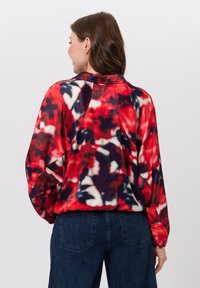Rood en marineblauw gebloemd patroonsweater met een geribbelde textuur, een relaxte pasvorm en elastische mouwen. Draagt met donkerdenim jeans.