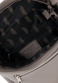 Light grey leather handbag interior with black fabric lining, featuring a zippered pocket and logo accents throughout.