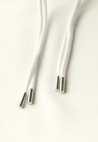 Cordons blancs avec des embouts métalliques sur un fond de tissu lisse et de couleur claire. Les embouts ont une forme cylindrique et une finition brillante.