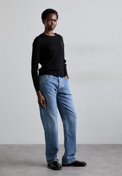 Black ribbed sweater, light blue baggy jeans, and black shoes. The sweater has long sleeves; the jeans feature a five-pocket design.
