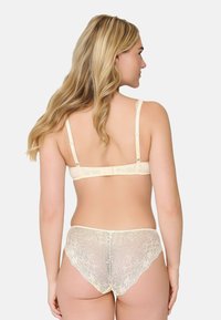 Sujetador beige con encaje y braguitas a juego vistos desde atrás, con tirantes ajustables y textura suave.