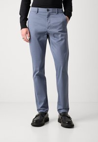 Pantalones azul claro de tela suave, con un diseño de pierna recta, bolsillos frontales y cierre de botón. Llevados con zapatos negros.