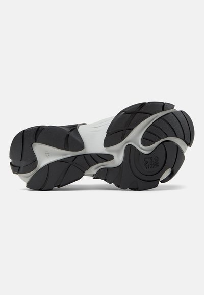 Semelle d'une chaussure de sport avec une bande de roulement en caoutchouc noir et gris présentant des rainures courbes et des motifs circulaires pour l'adhérence.