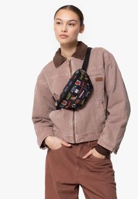 Black fanny pack with colorful comic-style prints, rectangular shape, and adjustable strap, worn over a beige, corduroy-collared jacket.