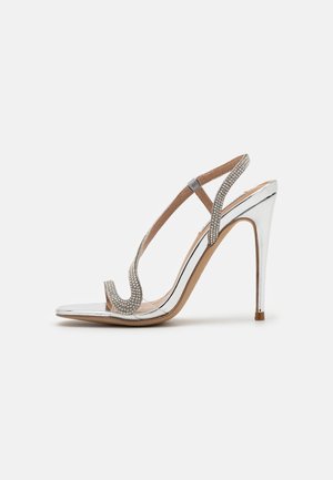 Sandale à talon haut argentée avec talon stiletto, lanières transparentes et ornements en strass le long de la bride en T et de la zone des orteils.
