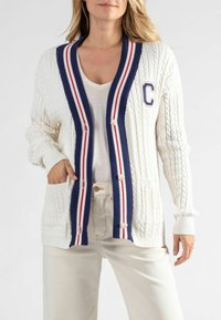 Crème kabelbrei cardigan met marineblauwe en rode gestreepte ribborde, knoopsluiting en zakken. Voorzien van een letter "C" embleem op de borst.