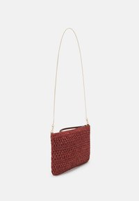 Borsa rettangolare all'uncinetto di un rosso scuro con una superficie texturizzata. Presenta una sottile tracolla in oro e un manico in pelle marrone per il trasporto.