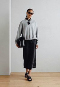 Sivá mikina s textúrovaným logom, čierna maxi sukňa, čierne šľapky a čierna kabelka. Modelka nosí slnečné okuliare a vzorovaný šál.