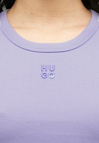 Λιλά ριμπ μπλουζάκι χωρίς μανίκια με στρογγυλή λαιμόκοψη, με κεντημένο λογότυπο "HUGO" σε σκουρότερες και ανοιχτότερες αποχρώσεις του μωβ.