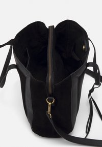 Sac seau en daim noir avec panneaux latéraux en cuir, fermeture éclair dorée et bandoulière réglable. L'intérieur est doté d'une doublure noire lisse.