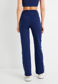 Marineblauwe sportbroek met een aangesloten taille en uitlopende benen, voorzien van witte zijstrepen en een gladde, rekbare stof.