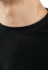 Black cotton t-shirt featuring a ribbed crew neckline, smooth texture, and a close-up view emphasizing fabric and stitching details.