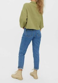 Green textured oversized top paired with light blue high-waisted jeans and beige lace-up ankle boots. The outfit features a relaxed fit.