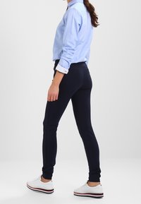 Marina blå tights i elastiskt material med en smoothing textur, smal silhuett och sidofickor, kombinerat med en ljusblå skjorta och vita sneakers.