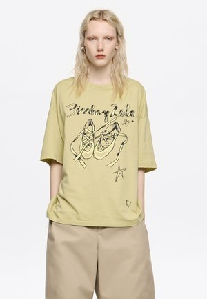 Jasnożółta, oversize'owa koszulka z czarnym rysunkiem butów i gwiazd. Wykonana z miękkiej bawełny, z małym detalem w kształcie serduszka na dolnym brzegu.