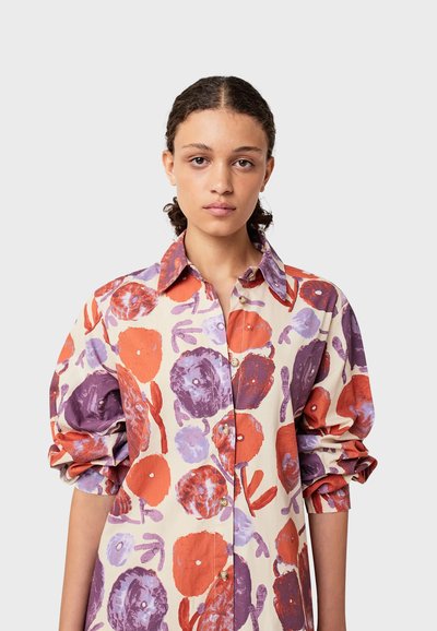 Camicia con bottoni di colore crema con audaci motivi floreali in rosso e viola. Presenta un colletto classico e maniche a sbuffo arricciate.