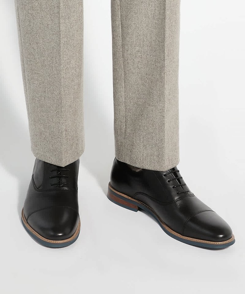 Chaussures habillées en cuir noir portées avec un pantalon gris clair, vues de face et de côté sur fond blanc.