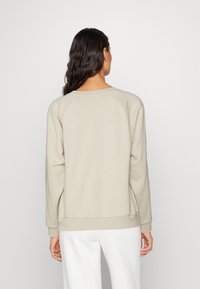 Felpa beige chiaro con maniche raglan, polsini e orlo a coste. Tessuto morbido e testurizzato con scollatura a girocollo. Design semplice, senza decorazioni.