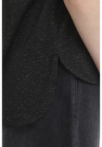 Mustrilise triibuga särke külgvaade, kus allservas on väike külje lõhik, kantud tume teksapükste kohal ning paljas käsi on nähtav.