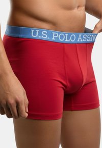 Red boxer briefs made of soft material with a light blue elastic waistband featuring the text "U.S. POLO ASSN." prominently displayed.