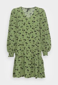 Vestido verde com decote em V, mangas bufantes longas e saia em camadas. O padrão inclui cerejas pretas no tecido com uma textura suave.