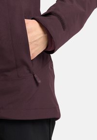 Giacca color bordeaux realizzata in un materiale liscio e impermeabile. Presenta una tasca laterale con zip e un dettaglio sul polsino in velcro per la regolazione.