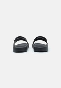 Sandales noires à semelle plate et deux brides supérieures. Fabriquées en matériau lisse et flexible, avec un design minimaliste et sans motifs.