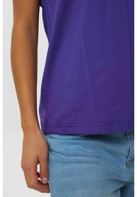 Violetti puuvillainen lyhythihainen t-paita, jossa ommellut helmareunat. Yhdistetty vaaleansinisiin farkkuihin.