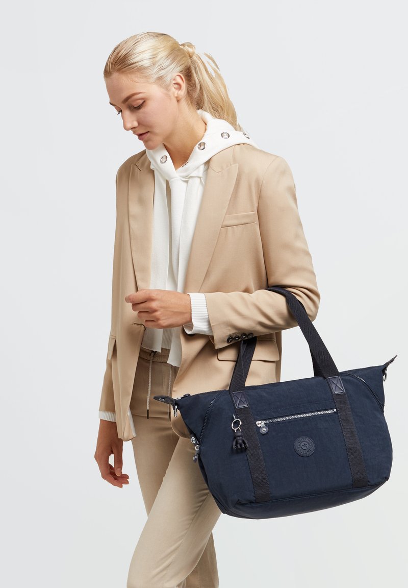 Marineblauwe stoffen totebag met zwarte accenten, een voorzak met rits, dubbele handvatten en een rond logo. Lichtgewicht ontwerp met een gestructureerde afwerking.