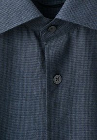 Camisa de vestir de color azul oscuro con patrón, con un cuello clásico, que presenta un cierre de botones y una tela sutilmente texturizada.