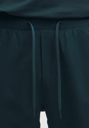 Temno zelene kratke hlače z elastičnim pasom in nastavljivimi vrvicami, izdelane iz lahkega blaga, s tekočo teksturo in minimalnimi detajli.