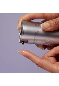 Silberne, zylindrische Flasche, die in der Hand gehalten wird und eine kleine Menge klarer Flüssigkeit auf die Fingerspitzen abgibt, mit aufgedrucktem Text und einem glänzenden Akzent.