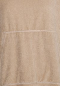 Felpa beige con un tessuto morbido e текстurizzato, caratterizzata da una tasca frontale centrale e cuciture in vista. Design semplice, senza motivi o accenti.