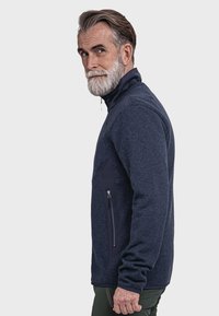 Navy-Fleecejacke mit hohem Kragen, einem mit Reißverschluss versehenen Brusttasche und strukturiertem Stoff. Hat kontrastierende dunkle Akzente an der Tasche.