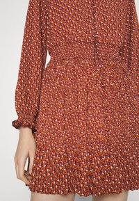 Vestido rojo con estampado floral, mangas abullonadas, cintura elástica y dobladillo con volantes; presenta un pequeño patrón geométrico en todo el vestido.