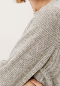 Maglione a maglia grigio chiaro con un tessuto testurizzato, caratterizzato da maniche lunghe e scollatura rotonda. Variazioni sottili di colore in tutto il capo.