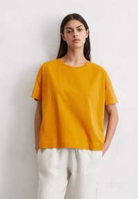 Geel katoenen t-shirt met korte mouwen, ronde hals en een ontspannen pasvorm. Gepaard met lichte, loszittende linnen broeken.