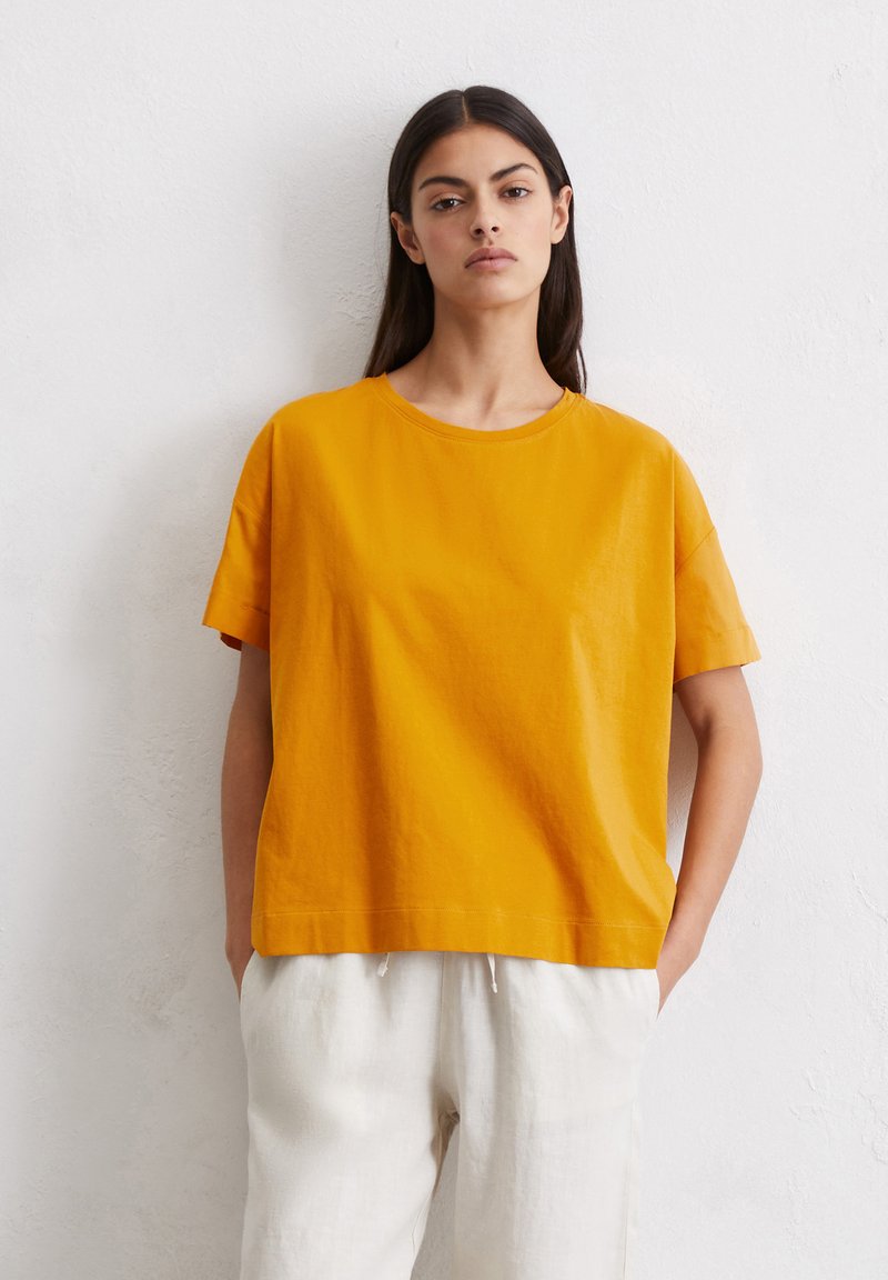 Geel katoenen t-shirt met korte mouwen, ronde hals en een ontspannen pasvorm. Gepaard met lichte, loszittende linnen broeken.