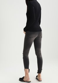 Svart ribbad långärmad topp som matchas med grå smala jeans med slitna detaljer, fransade fållar och svarta sandalettsskor.