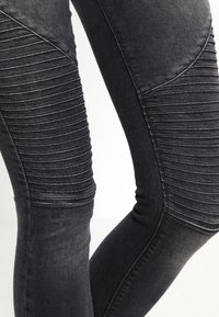 Pantalones de mezclilla negros con detalles acanalados en las rodillas, ajuste entallado y un acabado suave y texturizado.